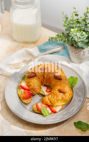 Appetitliches Croissant mit frischen Erdbeeren, Mandeln, Milch in einem Krug. Französisches Frühstück für eine Person. Nahaufnahme. Kochblog, Rezeptbuch, Restaurant Stockfoto