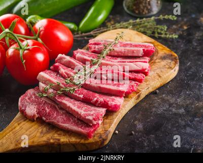 Kochen Steaks aus Bio-Fleisch vom Bauernhof. Auf einem hölzernen Schneidebrett, Steaks mit einem Zweig Rosmarin, Gemüse auf dunklem Hintergrund. Stockfoto