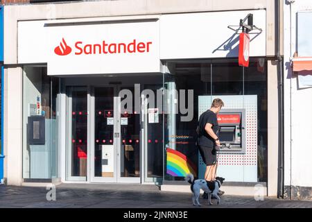 Santander Bank, eine Filiale der Bank in der Hauptstraße, mit einem Mann, der den Geldautomaten benutzt, Großbritannien Stockfoto