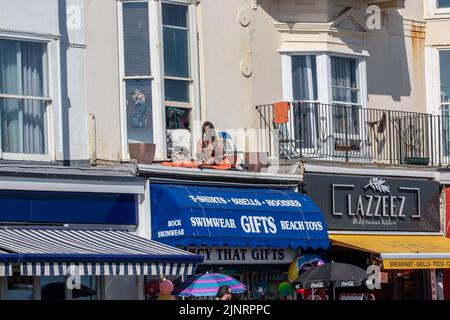 Brighton, Großbritannien. 13. August 2022. Tausende strömten diesen Samstag nach Brighton Beach und machten das Beste aus dem heißen Wetter. Ein See mit roten Schirmen (gesponsert von Walls Ice Cream) kann gesehen werden, die sich von Brighton bis Hove erstrecken Kredit: @Dmoonuk/Alamy Live News Stockfoto