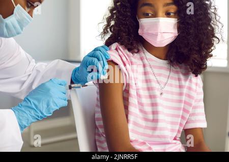 Afroamerikanisches Mädchen in medizinischer Gesichtsmaske bekommt einen Impfstoff, der sie vor Viren schützt Stockfoto