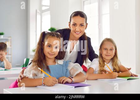 Porträt einer Lehrerin mit zwei kleinen Schülerinnen, die während des Unterrichts am Schreibtisch im Klassenzimmer sitzen. Stockfoto