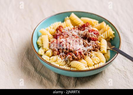 Bolognese Pasta in blauer Platte auf hellem Hintergrund. Traditionelles italienisches Gericht Stockfoto