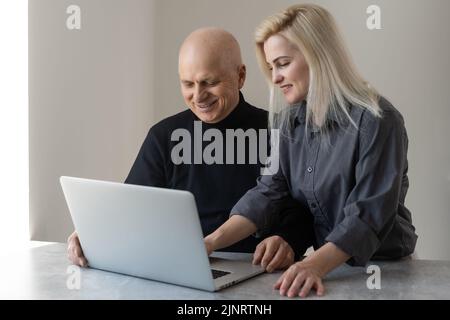 Frontansicht Happy Elderly 70s grauhaariger Mann lernt mit Hilfe von Computersoftware mit fürsorglicher erwachsener Tochter, älteren Menschen im Ruhestand und moderner Technologie Stockfoto