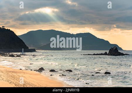 Das Sonnenlicht, das in der Abenddämmerung durch die Wolken am Sunset Beach filtert, führt zum Meoto IWA-Paar des Sakurai Futamigaura, dem von einem Heiligen geschützten Felsen Stockfoto