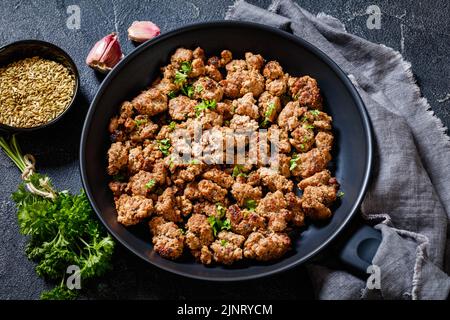 Gebratene italienische Wurst aus frisch gemahlenem Schweinefleisch und Gewürzen in schwarzer Schüssel auf Betontisch Stockfoto