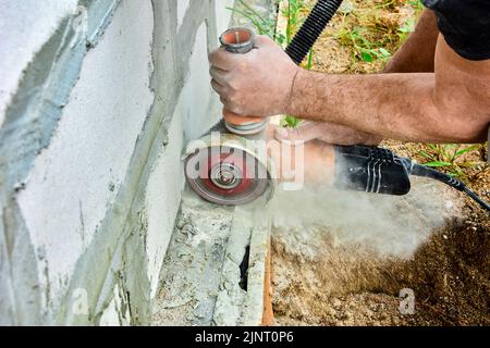 Schneiden von Mauerwerk mit Winkelschleifer und Betonsäge. Elektrische Hand-Elektrowerkzeug für Trockenschnitt erzeugt Wolke von Staub gefährlich für die Gesundheit. Stockfoto