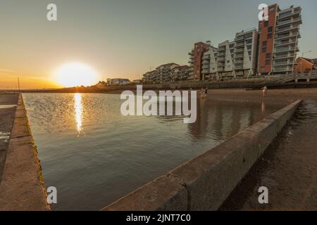 Southend on Sea, Großbritannien. August 2022. Eine ruhige Küstenszene bei Sonnenuntergang mit einem Gezeitenbecken oder einer Meeresmauer im Vordergrund, mit goldenem Licht, das vom Wasser reflektiert wird. Moderne Wohnhäuser säumen die Uferpromenade im Hintergrund und veranschaulichen den Kontrast zwischen natürlicher Schönheit und städtischer Entwicklung. Sonnenuntergang am Chalkwell Beach, in der Nähe von Southend on Sea. Bei Temperaturen um 25 Grad nutzen viele Leute den kühleren Abend. Penelope Barritt/Alamy Live News Stockfoto