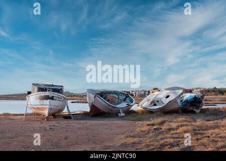 Schäbiges Schrott-Fischerboot. Alte Fischerboote laufen auf Grund. Verschrottete kleine Schiffe unter blauem Himmel und Wolken Stockfoto