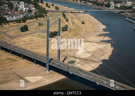 Düsseldorf, NRW, Deutschland, 13.. August 2022. Ungewöhnlich ist, dass ein Großteil der Rheinkniebrücke und ihrer Zufahrtsstraßen derzeit auf trockenem, vertrockneten Land stehen. Der Rhein, eine der verkehrsreichsten Binnenwasserstraßen der Welt, wurde stark von der anhaltenden Dürre und den daraus resultierenden niedrigen Wasserständen beeinflusst, die durch eine längere Hitze von bis zu 40 Grad und sehr wenig Regen in den letzten Wochen verursacht wurden. Die Schifffahrtsstraße hat sich erheblich verengt und den Verkehr verlangsamt, die meisten Schiffe mussten auch ihr Frachtgewicht erheblich reduzieren, was zu Lieferproblemen und höheren Schiffspreisen führte. Stockfoto