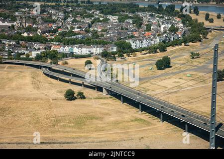 Düsseldorf, NRW, Deutschland, 13.. August 2022. Ungewöhnlich ist, dass ein Großteil der Rheinkniebrücke und ihrer Zufahrtsstraßen im Vorort Oberkassel derzeit auf trockenem, vertrockneten Land steht. Der Rhein, eine der verkehrsreichsten Binnenwasserstraßen der Welt, wurde stark von der anhaltenden Dürre und den daraus resultierenden niedrigen Wasserständen beeinflusst, die durch eine längere Hitze von bis zu 40 Grad und sehr wenig Regen in den letzten Wochen verursacht wurden. Die Schifffahrtsstraße hat sich erheblich verengt und den Verkehr verlangsamt, die meisten Schiffe mussten auch ihr Frachtgewicht erheblich reduzieren, was zu Lieferproblemen und höheren Schifffahrtskosten führte Stockfoto