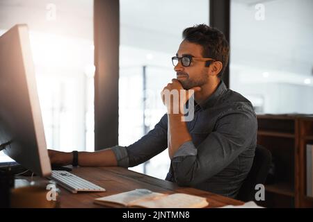 Er zeigt Tag und Nacht Hingabe. Ein junger Geschäftsmann, der spät am Computer in einem Büro arbeitet. Stockfoto