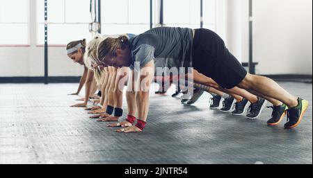 Gym - die Station für die Transformation des Körpers. Eine Gruppe junger Menschen, die Liegestütze in einem Fitnessstudio machen. Stockfoto