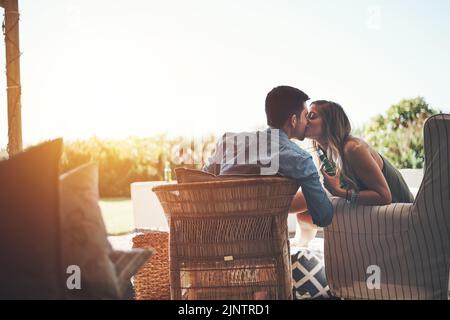 Nur für Ihre Lippen. Rückansicht eines liebevollen jungen Paares, das sich küsst, während es auf der Terrasse ein paar Biere genießt. Stockfoto