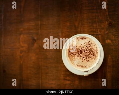 Der perfekte Start in den Morgen. Eine frisch gebrühte Tasse Kaffee, die in einem Restaurant auf einem Tisch neben dem eigenen steht, ist in einem hohen Winkel aufgenommen worden. Stockfoto