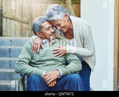 Ich bin so gesegnet, Sie in meinem Leben zu haben. Ein fröhlicher älterer Mann saß in einem Rollstuhl, während er tagsüber von seiner liebevollen Frau draußen zu Hause festgehalten wurde Stockfoto