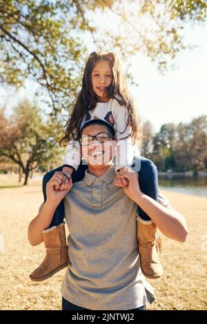 Im ihr großer Bruder beschützt sie und spielt mit ihr. Ein Teenager-Junge trägt seine entzückende kleine Schwester auf seinen Schultern. Stockfoto