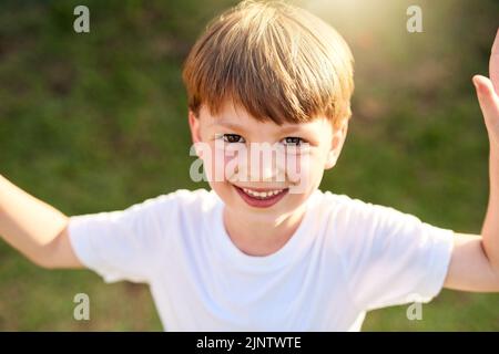 An einem sonnigen Tag lächelt Sunshiny. Porträt eines entzückenden kleinen Jungen, der draußen spielt. Stockfoto