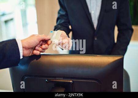 Zahlung für unsere Buchung. Ein nicht erkennbarer Geschäftsmann, der eincheckt und mit einer Kreditkarte in einem Hotel zahlt. Stockfoto