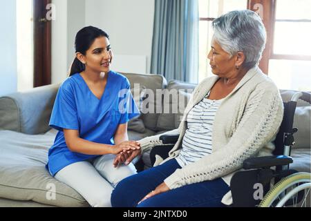 Bleibt nur optimistisch und alles wird in Ordnung sein. Eine besorgt aussehende ältere Frau sitzt in einem Rollstuhl, während eine Krankenschwester ihre Hand hält Stockfoto