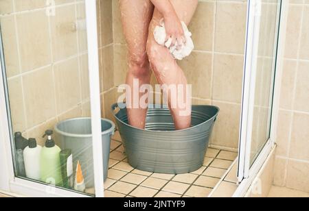 Sie werden vom Wassersparen profitieren, das werden wir alle. Eine unkenntliche Frau, die in einem Eimer wäscht, der zu Hause in die Dusche gestellt wurde. Stockfoto