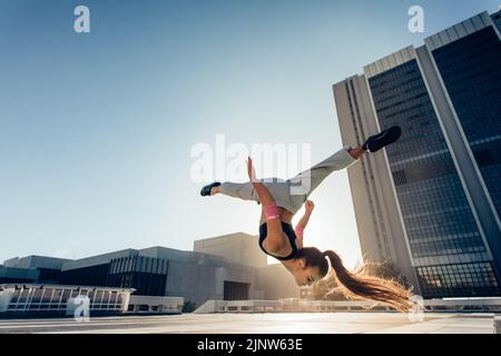 Frau macht Frontflip im Freien in der Stadt. Urbane Sportlerin in Aktion übt Parkour und Flashkick. Stockfoto