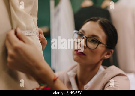 Junge Frau Schneiderin nimmt Messungen von Kleid an Schaufensterpuppe in ihrem Studio. Asiatische Mode-Designer Anpassung Kleid auf ein Modell. Stockfoto