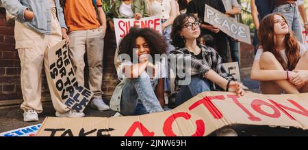 Fröhliches Teenager-Mädchen, das mit einer Gruppe JugendfriedensaktivistInnen an der Kamera lächelt. Multiethnische junge Menschen mit Plakaten und banne Stockfoto