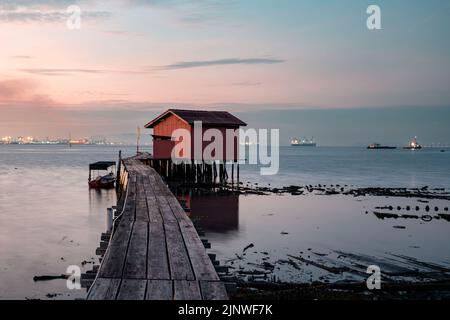 Blick bei Sonnenaufgang auf die Holzbrücke und den Hintergrund des roten Hauses am Clan Tan Jetty, einem der Touristenattraktionen in Georgetown, Penang, Malaysia. Stockfoto