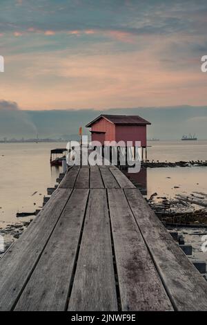 Blick bei Sonnenaufgang auf die Holzbrücke und den Hintergrund des roten Hauses am Clan Tan Jetty, einem der Touristenattraktionen in Georgetown, Penang, Malaysia. Stockfoto