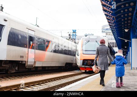 Junge Frau und kleines Mädchen, schöne Tochter, auf einem Bahnhof. Kind und Frau warten auf den Zug und freuen sich über eine Reise. Menschen, Reisen, Familie Stockfoto