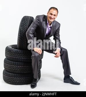 In voller Länge Porträt einer jungen Geschäftsmann, lehnend auf einem Haufen von Autoreifen auf weißem Hintergrund Stockfoto