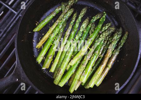 Spargel mit Zitronenschale, gegrillt im Freien in einer gusseisernen Pfanne Stockfoto