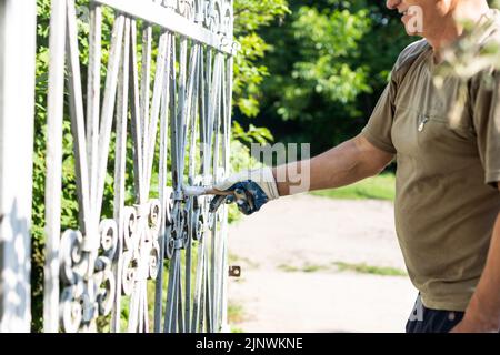 Hand des Auftragnehmers mit Pinsel, die Metallzaun malen. Stockfoto