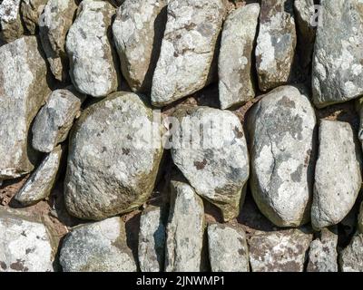 Mauerwerk als Hintergrund. Ein Fragment eines Zauns aus unbehandelten Steinblöcken, Textur. Graue und braune Steine Stockfoto