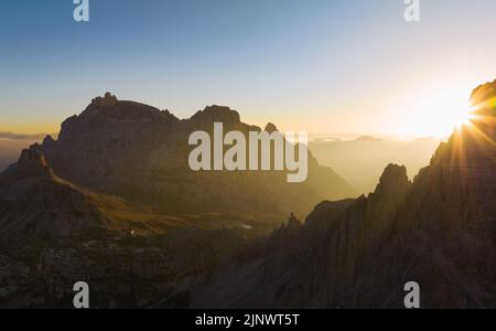 Blick von oben, atemberaubende Luftaufnahme einer Bergkette bei einem schönen Sonnenaufgang mit einer Berghütte in der Ferne. Stockfoto