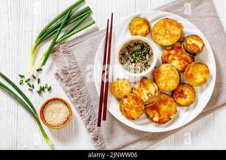 Hobak Jeon, gebratene Zucchini in Eierteig serviert mit Soja-Dipping-Sauce auf Teller mit Essstäbchen auf weißem Holztisch, koreanische Küche, horizontal Stockfoto