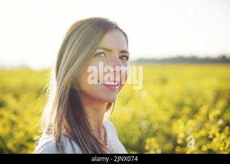 Porträt einer jungen Frau mit langen Haaren, gelbem Blumenfeld und Sonnenlicht hinter ihr Stockfoto