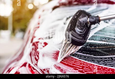 Detail der dunkelroten Heckscheibe im Autowaschgang. Pinsel hinterlässt Striche in weißer Seife und Shampoo-Schaum Stockfoto