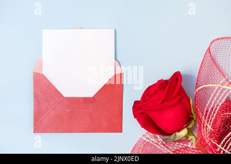 Draufsicht auf roten Umschlag und weiße leere Karte mit schöner Rose auf hellblauem Hintergrund, Kopierraum Stockfoto