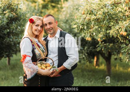 Junges Paar in serbischer Tradition, das einen Korb mit frischen Birnen hält Stockfoto