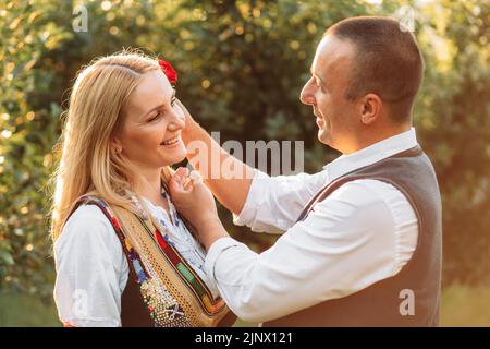 Ehemann und Ehefrau in serbischer traditioneller Kleidung. Ehemann setzte stieg hinter seine Frau Ohr Stockfoto