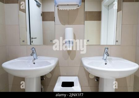 Zwei symmetrische Waschbecken in einer modernen öffentlichen Toilette mit Papiertüchern und Seifenschalen Stockfoto