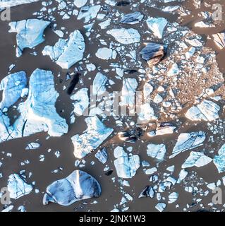 Blick von oben auf blaue Eisberge in der Fjallsarlon-Gletscherlagune im Süden Islands. Das umgebende Wasser ist aufgrund vulkanischer Schlammablagerungen braun. Dron Stockfoto