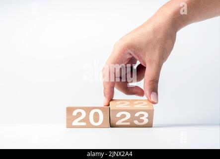 Nahaufnahme Hand Umblättern der 2022 bis 2023 Jahre Zahlen Kalender auf Holzwürfelblöcke für die Vorbereitung der neuen Jahr ändern, beginnen und neue Geschäfte zu starten Stockfoto