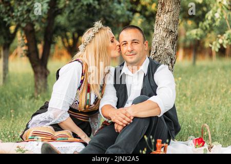 Ehemann und Ehefrau in serbischer traditioneller Kleidung, sitzen unter einem Baum Stockfoto