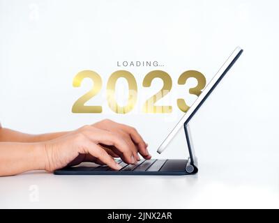 Wird auf 2023 Frohes neues Jahr. geladen Der Kalender mit 2023 Jahreszahlen erscheint auf einem digitalen Tablet-Computer, wobei die Hände ihn auf weißem Hintergrund eingeben, um sich auf n vorzubereiten Stockfoto