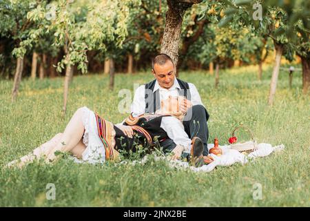 Ehemann und Ehefrau in serbischer traditioneller Kleidung, genießen unter einem Baum Stockfoto