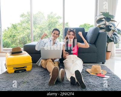 Glückliches asiatisches Paar bereit zu reisen, junger Mann und Frau, zeigen Erfolg, mit Laptop-Computer und digitalen Tablet zusammen für die Buchung von Flugtickets, t Stockfoto