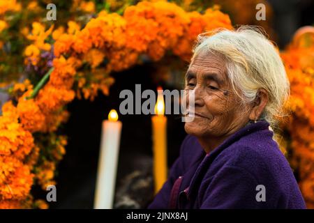 Auf dem mit Blumen geschmückten Grab auf einem Friedhof sitzt während der Feierlichkeiten zum Tag der Toten in Metlatónoc, Guerrero, eine indigene Frau aus Mixtec. Stockfoto